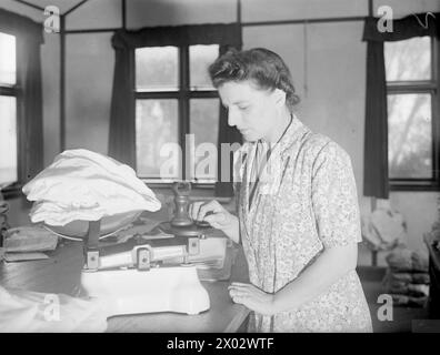 IN UN MAGAZZINO DI ABBIGLIAMENTO DELL'AMMIRAGLIATO. 17 OTTOBRE 1944, NAVAL STORES SOUTHERN AREA, GUILDFORD. GLI UFFICIALI E GLI UOMINI E LE DONNE DELLA ROYAL NAVY SANNO CHE STANNO OTTENENDO UN BUON RAPPORTO QUALITÀ/PREZZO QUANDO FANNO ACQUISTI NEI "PUSSERS STORES", IL SOPRANNOME DELLA MARINA PER IL DEPOSITO DI ABBIGLIAMENTO A TERRA O IN MARE. OGNI ARTICOLO DI ABBIGLIAMENTO DEVE SUPERARE UN DOPPIO TEST E VERIFICARE LA QUALITÀ, IL PESO E LA PRECISIONE DEL DESIGN PRIMA DI RAGGIUNGERE LA SALA DI EMISSIONE DELL'ABBIGLIAMENTO. - Signora e Sloggatt, pesando un fascio di biancheria intima WRNS, così tanti pezzi devono essere conformi alla 1lb Foto Stock