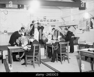 AL "SAILOR'S REST" DI HARWICH. 27 LUGLIO 1944, HARWICH. È STATA APERTA UNA VECCHIA STALLA CONVERTITA DA RATING IN UNA SALA DI RIPOSO E INFORMAZIONE. - Un sottufficiale Wren in servizio nel bagno per rispondere a domande, distribuire libri, ecc.. Foto Stock