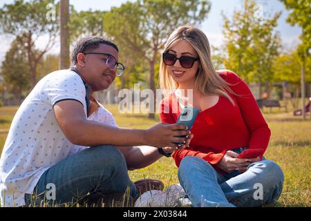 Felice coppia interrazziale che controlla il cellulare all'aperto. Foto Stock