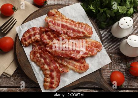 Fette di pancetta fritte, pomodori, prezzemolo e spezie su un tavolo rustico in legno, piano Foto Stock