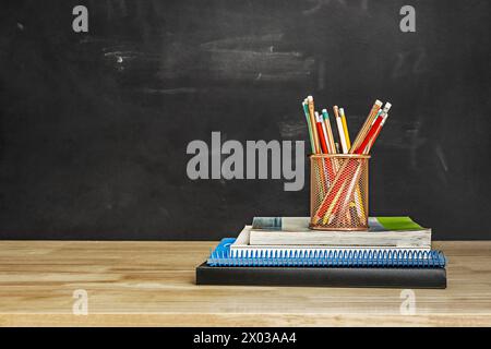 Un quaderno a spirale blu con altri libri e un secchio con matite sulla parte superiore Foto Stock