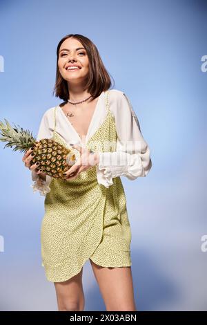 Una donna bruna che regala graziosamente un vivace ananas in un abito elegante. Foto Stock