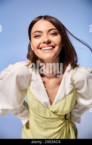 Una giovane donna gioiosa con i capelli bruna sorride brillantemente alla macchina fotografica, vestita con un vestito giallo brillante. Foto Stock