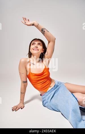 Una giovane donna con capelli bruna elegantemente vestita con un top arancione e una gonna blu in un ambiente da studio. Foto Stock