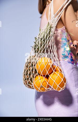 Una giovane donna con i capelli bruna regala felicemente una borsa piena di arance fresche in un vivace ambiente da studio. Foto Stock