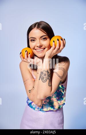 Una giovane donna con i capelli bruna tiene due arance davanti al viso in un ambiente da studio. Foto Stock