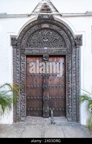 Una porta ad arco in legno finemente intagliato con chiocciole in ottone e una serratura in ottone ornata all'ingresso di una tradizionale casa araba. Foto Stock