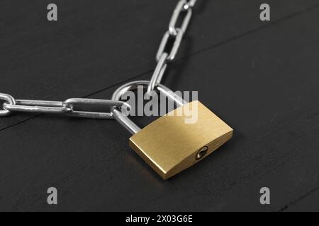 Lucchetto in acciaio con catena su tavolo in legno nero, primo piano Foto Stock