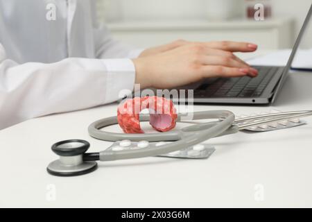 Endocrinologo che lavora a tavola, si concentra sullo stetoscopio e sul modello della ghiandola tiroidea Foto Stock