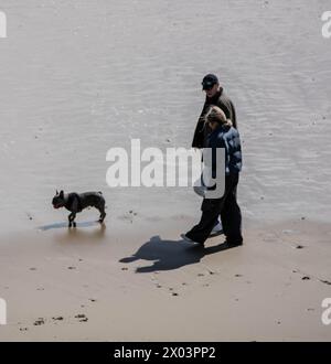 Bournemouth Dorset 9 apr 2024 Meteo britannico; i visitatori godono del sole primaverile nonostante i venti forti e il grande ondeggiamento dalle tempeste notturne. Coppia cane da passeggio, credito: Ian Davidson/Alamy Live News Foto Stock