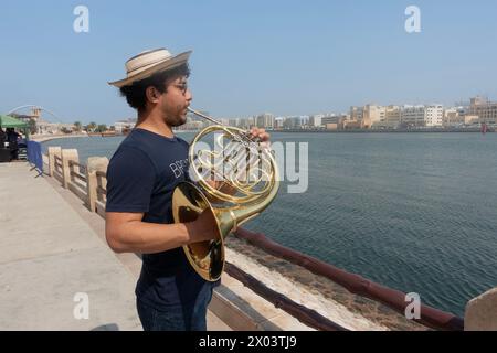 Giovane musicista che suona il corno francese sulla riva del torrente nel quartiere storico di al Shindagha, Dubai, Emirati Arabi Uniti. Foto Stock