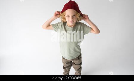 L'immagine mostra un giovane uomo con un cappello rosso brillante con capelli rossi che sta con sicurezza sui suoi piedi su uno sfondo grigio. I suoi occhi brillano da un Foto Stock