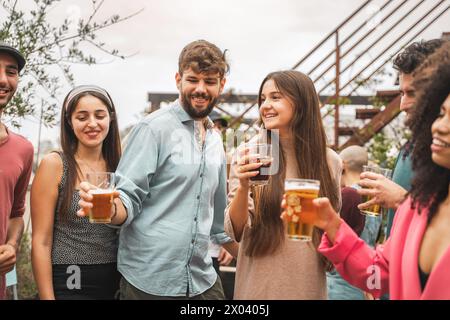 Un gruppo di giovani adulti condivide un brindisi allegro - amici rilassati che bevono e socializzano durante la riunione sul tetto - lo spirito della cultura giovanile, urbano c Foto Stock