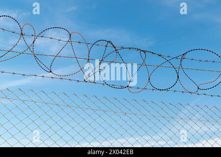 Una recinzione con filo spinato contro un cielo blu. Area riservata. Foto Stock