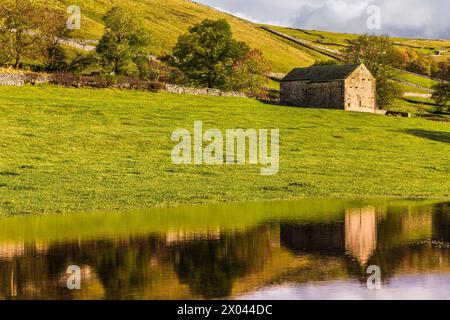 Fienile tradizionale in pietra riflessa in un campo allagato vicino a Kettlewell, Wharfedale, Yorkshire Dales, Inghilterra. Foto Stock