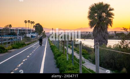 Un uomo che pedala su una pista ciclabile vicino a Marina del Rey, California, Stati Uniti, all'alba, con montagne nebbiose sullo sfondo e zone umide nelle vicinanze Foto Stock