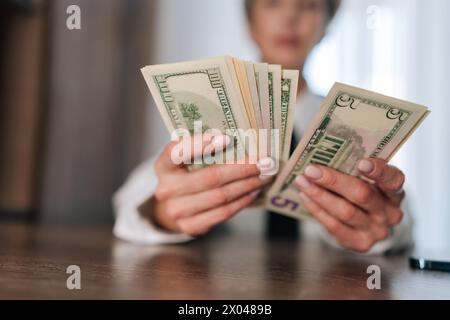 Obiettivo selettivo di una donna che conta denaro contante banconote da uno, cinque, dieci, venti e cento dollari sedute a tavola. Concetto di Foto Stock