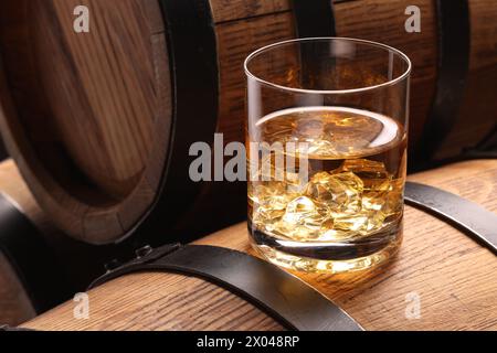 Whisky con cubetti di ghiaccio in vetro su botte di legno, primo piano Foto Stock