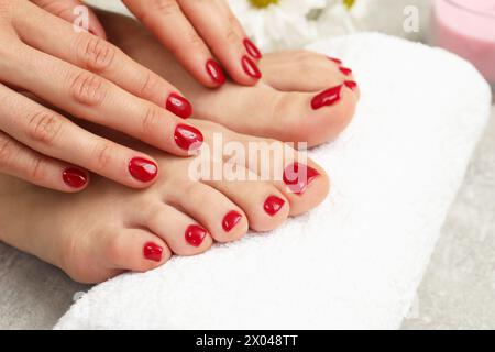 Donna che mostra eleganti unghie del piede dopo la procedura di pedicure e mani curate con smalto rosso su pavimento grigio, primo piano Foto Stock