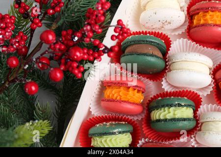 Diversi gustosi macaron natalizi in scatola e decorazioni natalizie sul tavolo, vista dall'alto Foto Stock