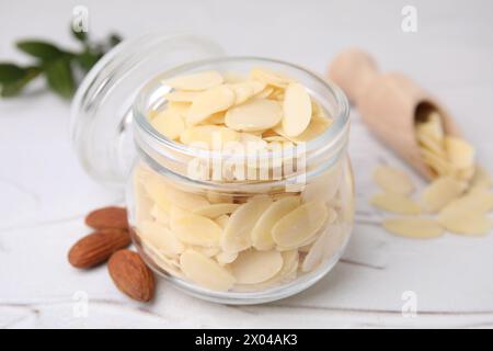 Fiocchi di mandorle fresche in vaso e noci su un tavolo bianco testurizzato, primo piano Foto Stock