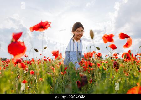 vista ad angolo basso della ragazza con camicetta azzurra in piedi nel campo dei papaveri contro il cielo luminoso Foto Stock