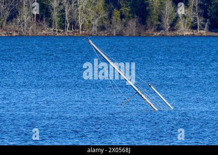 I montanti di una barca a vela affondata si attaccano ad un angolo dall'acqua blu. Foto Stock