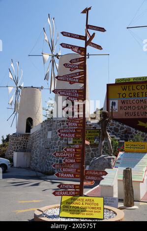 Ano Kera, Creta, Grecia - 06 29 2013: Un palo con le indicazioni che indicano la direzione e la distanza per le famose città di tutto il mondo davanti al greco bianco Foto Stock