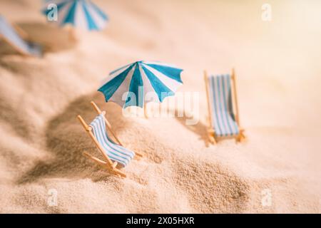 Lettini e ombrelloni a righe sulla sabbia gialla e pulita della spiaggia Foto Stock