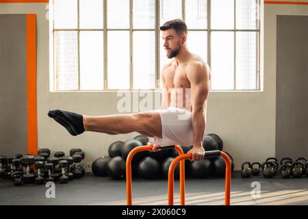 Vista laterale del muscolo maschile che fa L siedono su barre parallele esercizi di calistenica nel moderno fitness club Foto Stock