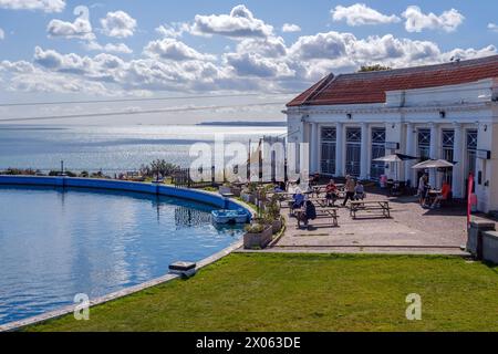 Diversi tavoli di persone mangiano all'aperto vicino alla piscina nautica Royal Esplanade, Ramsgate. Edificio Café sulla destra. Pedalò agganciato. Foto Stock
