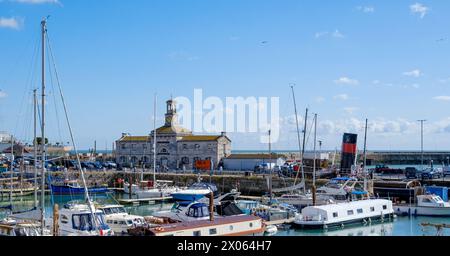 Il Ramsgate Royal Harbour è pieno di varie barche e yacht, sotto un cielo blu con soffici nuvole bianche. Edificio dell'orologio sullo sfondo. Foto Stock