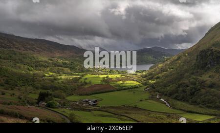 Le nuvole di Moody si stagliano su una lussureggiante valle verde, circondata dalle montagne di Snowdonia, Galles del nord, Regno Unito, con il sole che mette in risalto parti del vallone Foto Stock