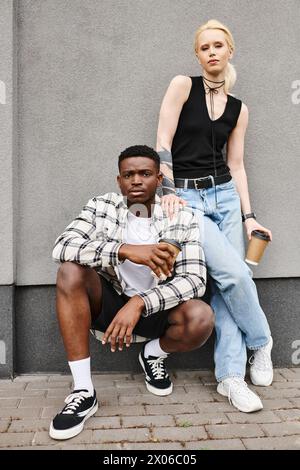 Una coppia felice, un uomo e una donna di origini diverse, posano insieme in una strada urbana vicino a un edificio grigio. Foto Stock