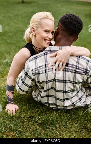 Una felice coppia multiculturale, un uomo afroamericano e una donna caucasica, che condividono un tenero abbraccio sull'erba in un parco. Foto Stock