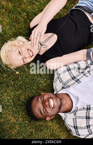 Un gioioso uomo afroamericano e una donna caucasica che giacciono insieme sull'erba verde, collegandosi in un tranquillo ambiente all'aperto. Foto Stock