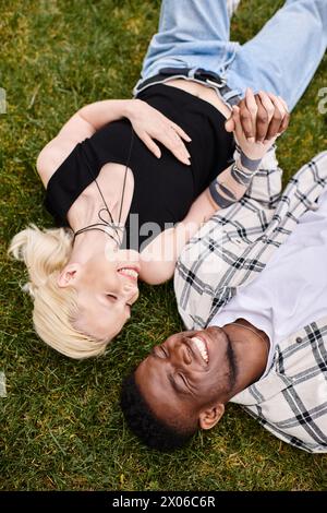 Una coppia felice e multiculturale, un uomo afroamericano e una donna caucasica, rilassatevi insieme, abbracciando la lussureggiante erba verde in un parco. Foto Stock