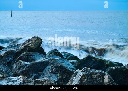 Massi di granito scuri contro le onde che si infrangono Foto Stock