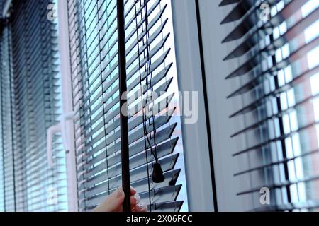 Con la mano, una donna gira una delle leve per controllare le tende di legno sulla finestra Foto Stock