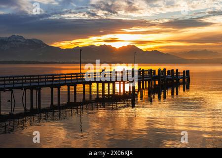 Luce dorata del tramonto del sole invernale sul molo deserto del piroscafo e sul panorama alpino, Germania, Baviera, Lago Chiemsee Foto Stock