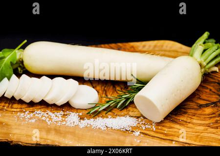 Ravanello da giardino (Raphanus sativus), due ravanelli su una tavola di legno, tagliati a fette di sale Foto Stock