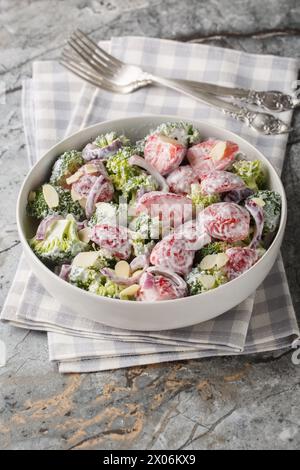 Insalata di broccoli, fragole, cipolla rossa e mandorle condita con yogurt da vicino in un piatto sul tavolo. Verticale Foto Stock