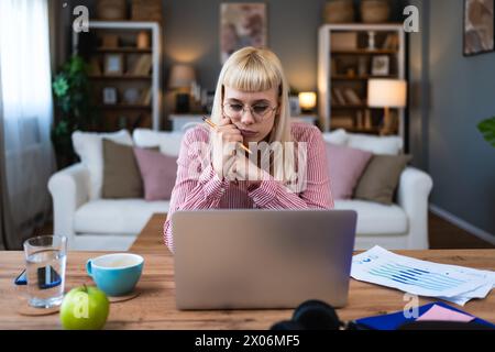 Giovane lavoratrice freelance malata che lavora a casa, lavora su un computer portatile. Telelavoro online, connessione wireless femminile con l'azienda, che esegue di Foto Stock