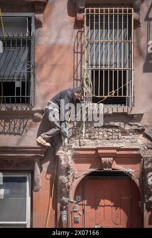 Un operaio edile in una posizione precaria rompe il cemento con il martello. Una ristrutturazione di una vecchia casa in Bedford Ave a Williamsburg, New York. Foto Stock