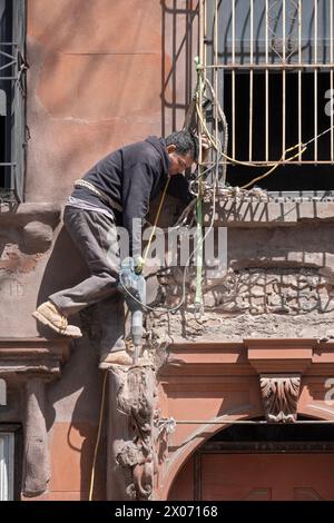 Un operaio edile in una posizione precaria rompe il cemento con il martello. Una ristrutturazione di una vecchia casa in Bedford Ave a Williamsburg, New York. Foto Stock