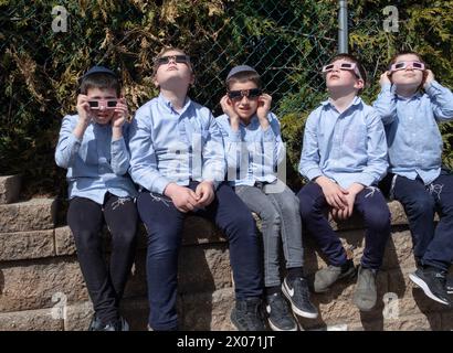 Un gruppo di ragazzi ebrei ortodossi guarda l'eclissi solare del 2024 dal cortile della scuola della loro yeshivah. Nella contea di Rockland, New York. Foto Stock