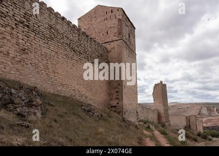 antico, alto muro di pietra e torre, parte di una fortezza, sotto un cielo nuvoloso con un ambiente arido. Foto Stock