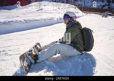 Uno snowboarder seduto sulla neve, facendo una pausa sulle piste da sci con vedute panoramiche. Foto Stock