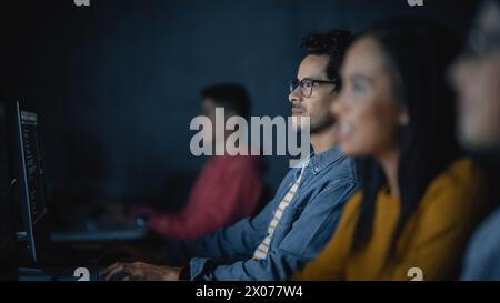 Gruppo multietnico di studenti di sesso femminile e maschile seduti nella sala del college, che collaborano a progetti scolastici su un computer. Giovani studiosi studiano, parlano, applicano competenze accademiche e conoscenze in classe. Foto Stock