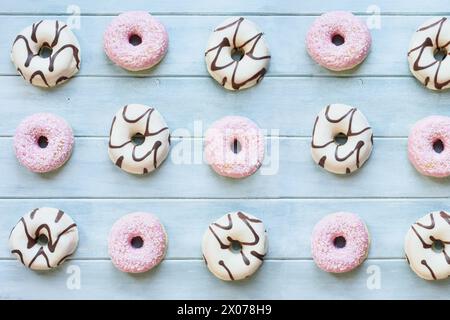 Posate di ciambelle alla vaniglia smerigliate con perline al cioccolato e ciambelle rosa fragola con fiocchi di cocco. Vista dall'alto del tavolo. Sfondo piatto Foto Stock